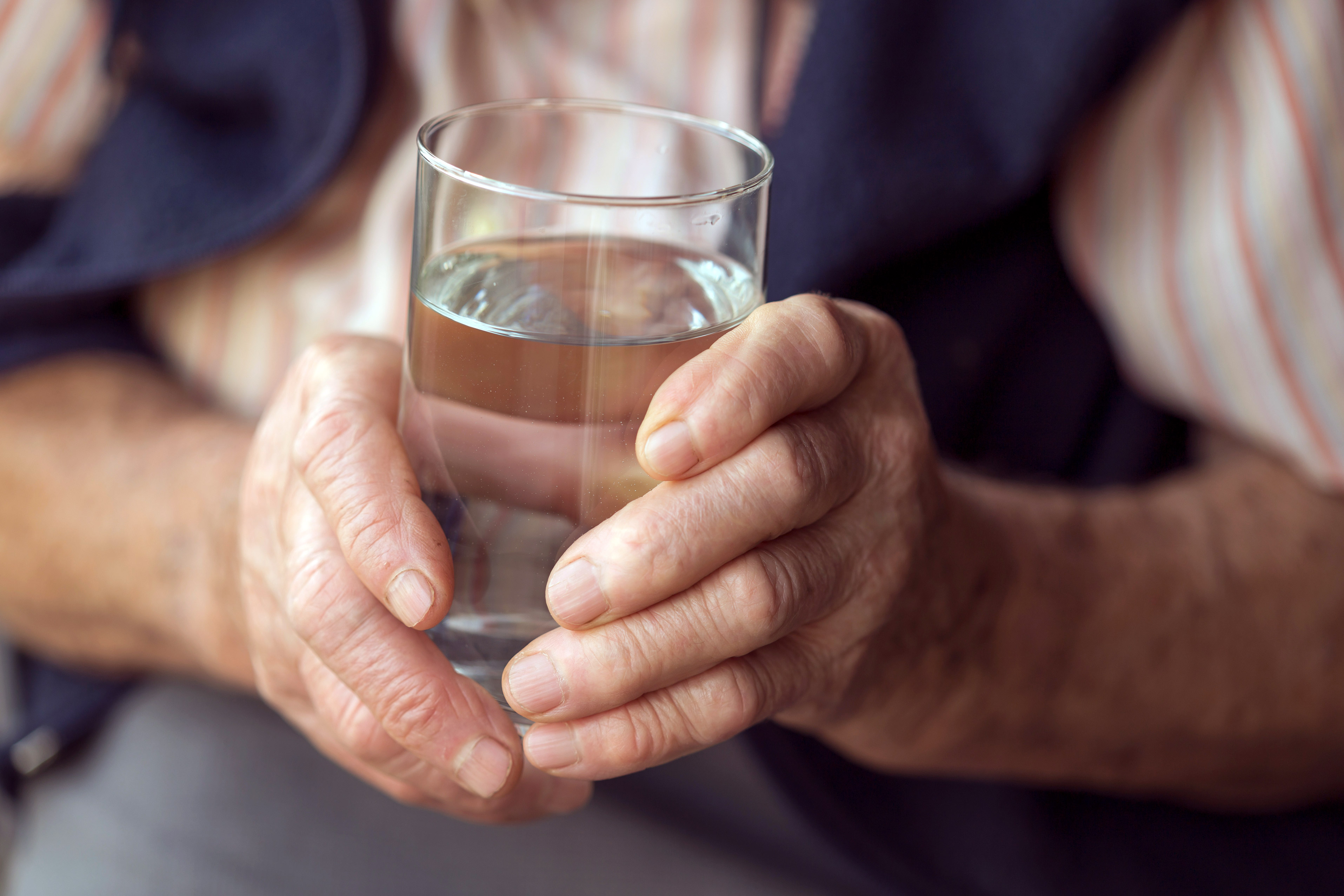 A glass of water being held in two hands by an elderly white person
